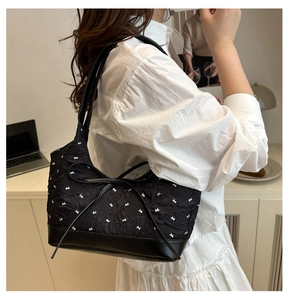 Detail of black quilted shoulder bag with white bow embroidery and leather base