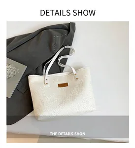 Detail of white woven textured tote bag with a brown logo patch and long shoulder straps