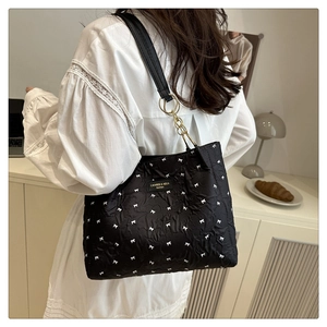 Détail du sac cabas matelassé noir avec motifs nœuds blancs et plaque métallique élégante