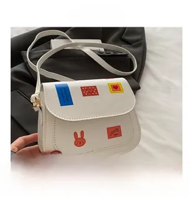 Détail du sac selle en cuir blanc avec imprimés timbres colorés et boucles dorées