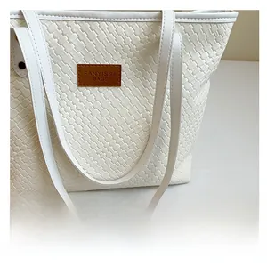 Detail showing white woven leather texture and a brown logo tag on a chic shoulder bag