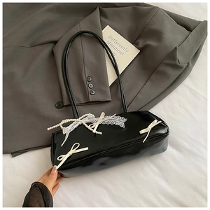Close-up of black glossy shoulder bag with white leather bows, lace, and pearl chain detail