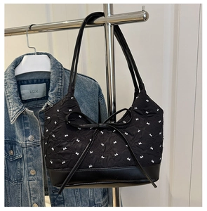 Detail of black quilted bucket bag with white bow embroidery and large leather ribbon