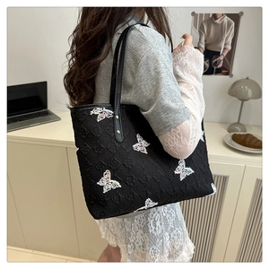 Detail of a black quilted tote bag with colorful butterfly embroidery and leather straps