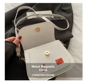 Détail du sac de selle blanc avec boucle magnétique dorée et écusson orange en cuir