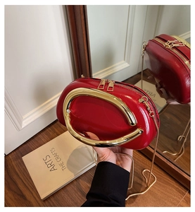 Detail of red round clutch bag featuring a gold semi-circular metal handle and leather texture