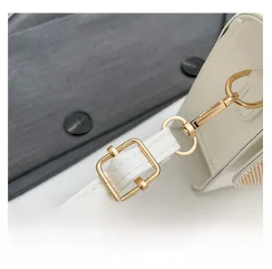 Detail of adjustable leather shoulder strap with gold metal buckles on a white bag