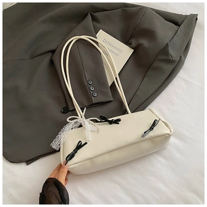 Detail of cream baguette bag with black bows and pearl lace charm on white fabric
