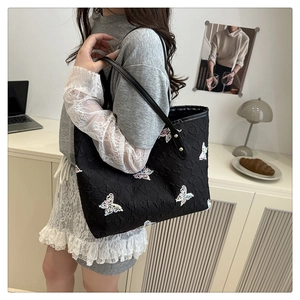 Detailed view of black tote bag with butterfly patterns on a shoulder-carried model