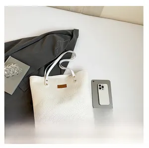 Detailed view of large white woven tote bag with brown patch next to a tablet and book