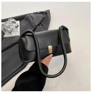 Close-up of matte black leather handbag featuring a glossy gold press-lock and twin handles