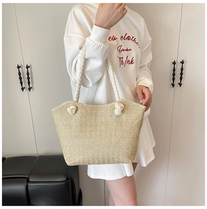 Close-up of woven straw tote bag with chunky white cotton rope handles and knot details