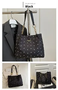 Detail of black quilted shoulder bag with bow embroidery and gold chain strap