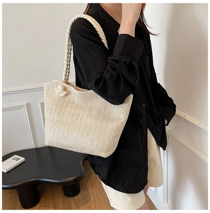 Close-up of cream woven straw tote bag with braided handles and herringbone texture