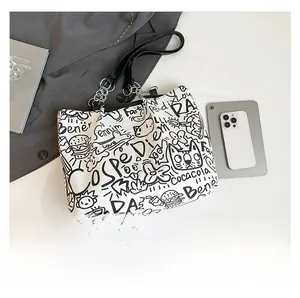 Detail showing graffiti prints and metal chain strap on white canvas tote bag