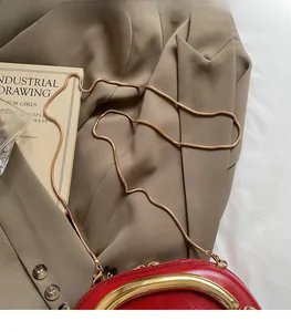 Detail of red glossy shoulder bag with golden metal handle and snake chain on khaki blazer