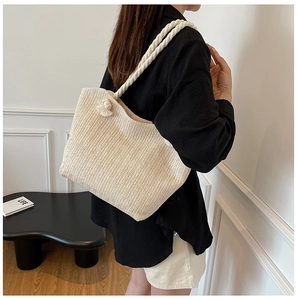Detail of hand-woven straw tote bag with thick cotton rope handles and tassel charm