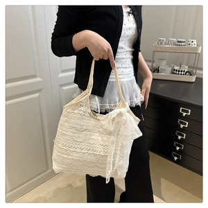 Detail of white lace tote bag featuring intricate floral patterns and large bow accent