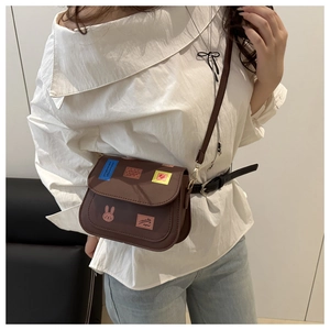 Close-up of brown crossbody bag with colorful patches and cute rabbit detail on model