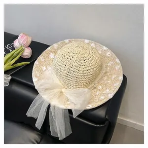 Detail of beige woven straw hat with white lace floral embroidery and tulle bow
