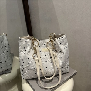 Chic cream tote bag with black bow print, pleated texture and gold metal ring handles