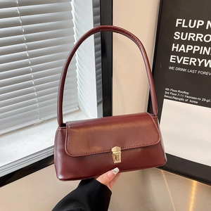 Deep red baguette shoulder bag with gold clasp shown against a modern interior backdrop