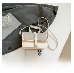 Detail of cream crossbody bag with glitter flap and twisted silver handle near phone