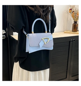 Close-up of light blue handbag featuring texture patchwork and golden D-buckle detail