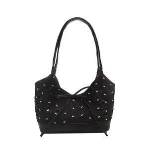 Elegant black shoulder bag with white bow pattern and leather bow detail on white backdrop