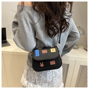 Dettaglio della borsa a sella nera con patch a cartoni animati colorati sulla patta