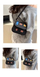 Detail of black crossbody bag with colorful cartoon patches and adjustable gold buckle