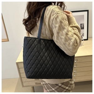 Detailed side view of black quilted tote bag with diamond stitching on leather shoulder strap