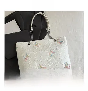 Detail of white quilted tote bag with colorful butterfly embroidery and silver chain strap
