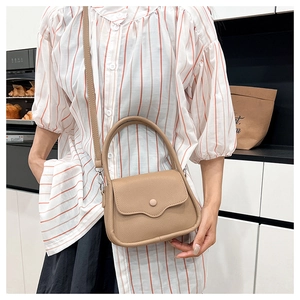 Close-up of khaki textured leather crossbody bag with wavy flap and round buckle