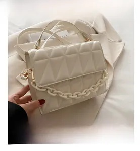 Close-up of white quilted crossbody bag featuring resin chain and gold hardware detail