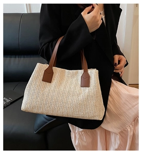 Detailed view showing the texture of a beige woven straw handbag with brown PU handles