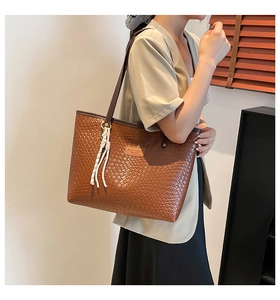 Detail of brown woven tote bag featuring textured leather surface and stylish tassel charm