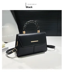 Detail of black woven handle and gold metal clasp on square leather crossbody bag