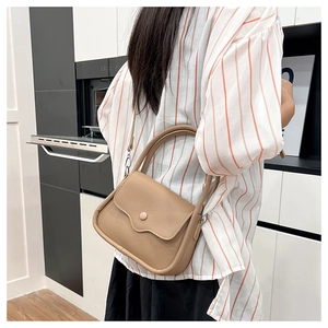 Model wearing a tan litchi pattern leather handbag with round flap and shoulder strap