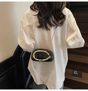 Detail of a black leather crossbody bag with a gold C-handle and chain strap on a model