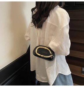 Detail of black oval crossbody bag featuring a bold golden C-shaped metal handle decoration