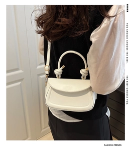Close-up of white PU leather saddle bag with unique knotted handle and slim strap