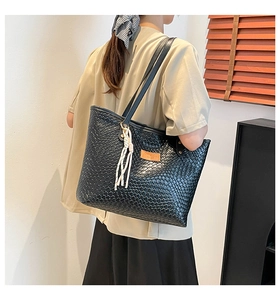 Close-up of black woven tote bag featuring white tassel charm and brown leather patch