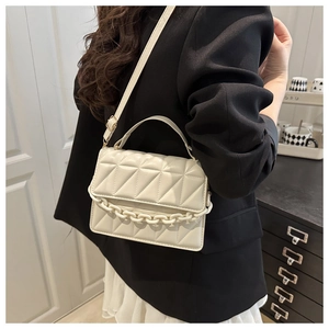 Détail du sac beige matelassé avec coutures triangulaires et poignée en grosse chaîne