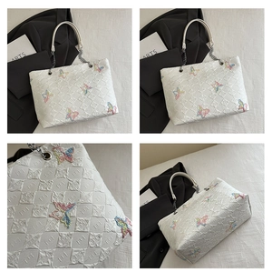 Detail of white quilted leather tote bag with colorful butterfly embroidery and chain strap