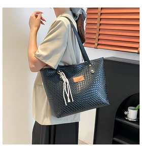 Detail of woven texture on large black tote bag with brown leather tag and tassel charm