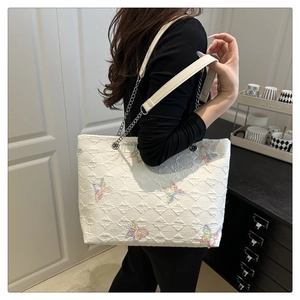 Detail of white quilted tote bag with colorful butterfly embroidery and chain strap