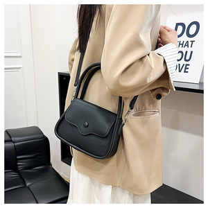 Detail of black lychee grain leather saddle bag on a model wearing a beige trench coat