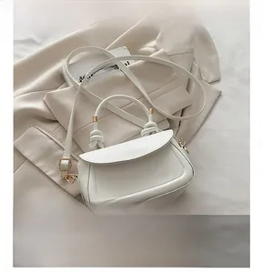 Detail of white handbag with knotted handle and phone for size reference on suit