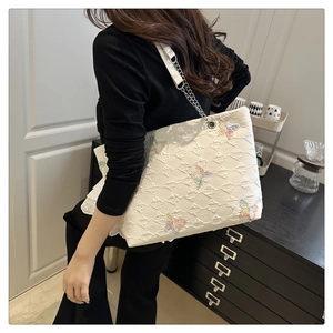 Detailed shot of white quilted tote bag with colorful butterfly sequins and chain strap